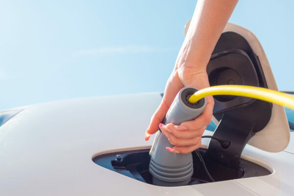 Female hand, opening a socket cover and plugging in the charger in an electric car at a charging station