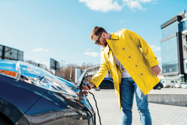 Stylish man in sunglasses disconnects the charging cable from his electric car